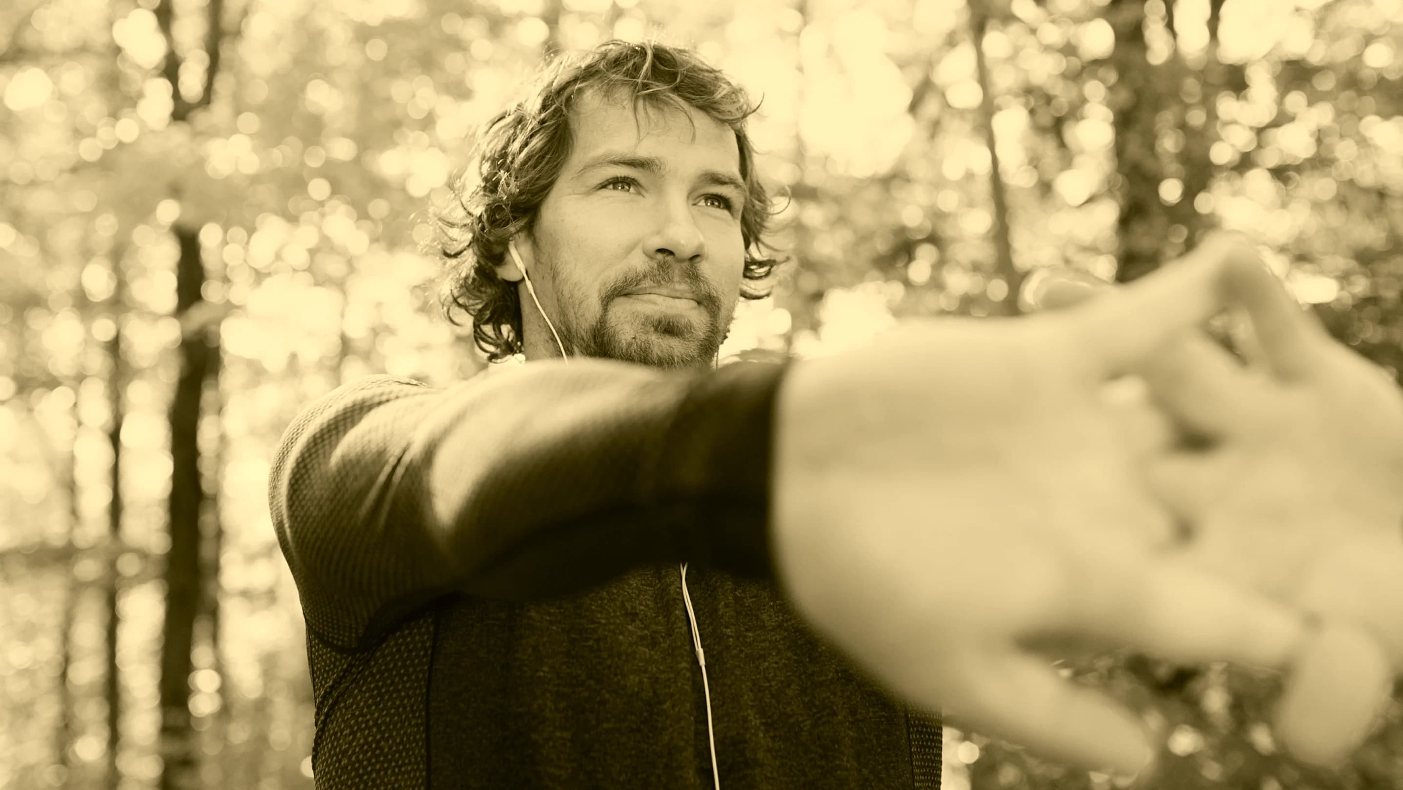 A man stretches outdoors among trees in warm sunlight.